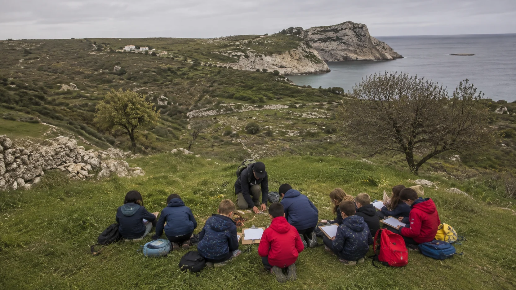 Educación ambiental: grupo de escolares de espaldas agachados alrededor de un monitor en el campo