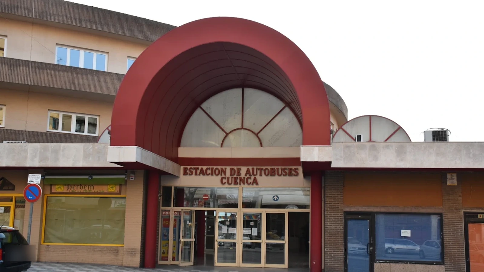 Entrada de la estación de autobuses de Cuenca: marquesina en arco de chapa granate sobre las puertas de cristal, con el rótulo de la estación bajo el arco