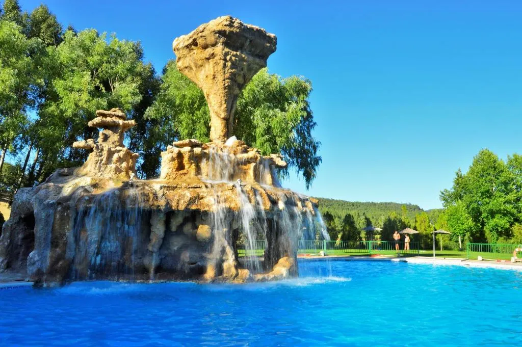 Piscina del Camping Caravaning Cuenca con cascada de piedra rodeada de pinos