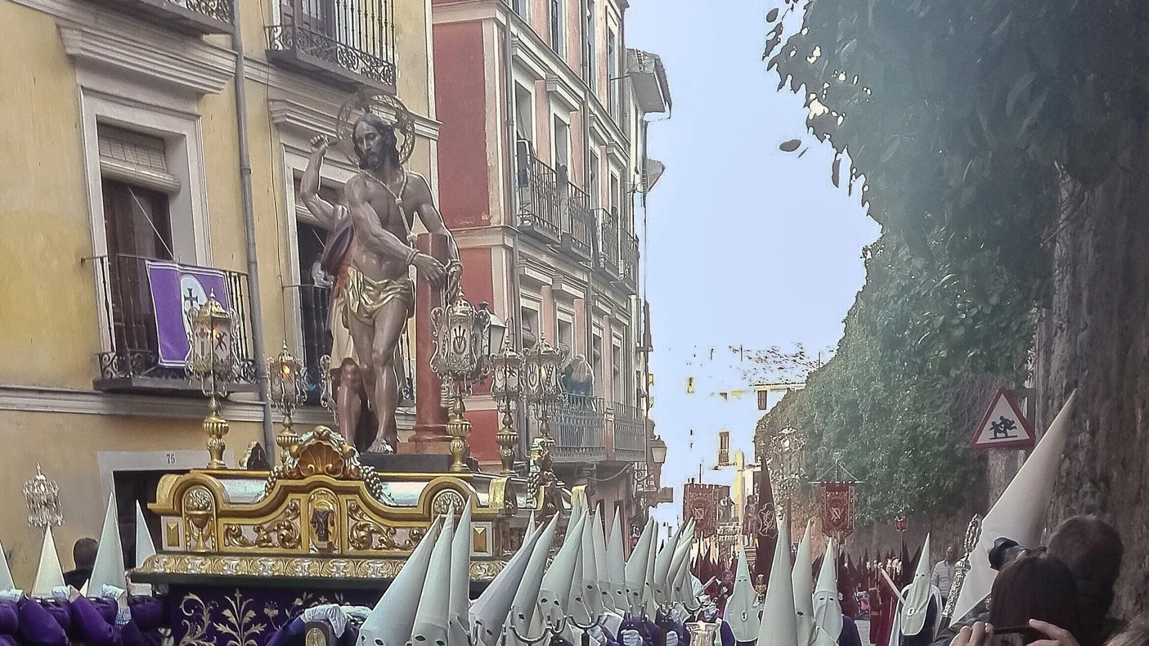 Procesión de encapuchados con faroles (tulipas) encendidos de noche por una calle empedrada