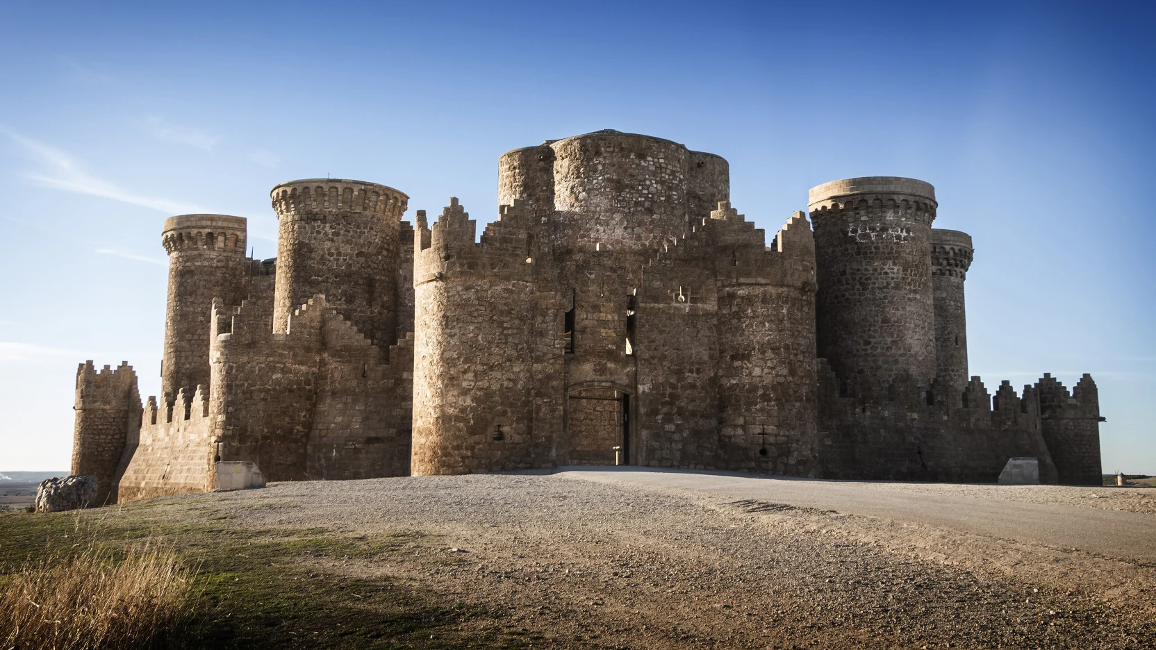 Silueta de un castillo medieval sobre un cerro pelado al atardecer
