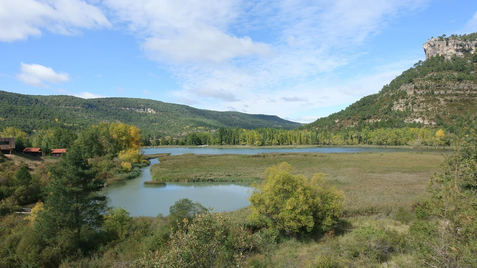 Laguna de aguas quietas con el pueblo de Uña al fondo bajo un farallón