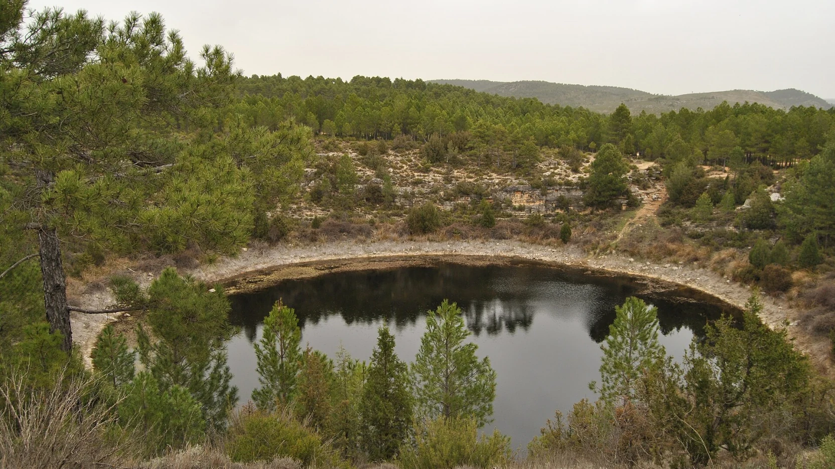 Laguna circular de agua verde encajada en paredes de roca, Cañada del Hoyo